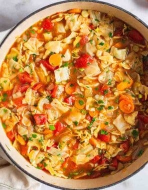 an overhead photo of a pot of detox cabbage soup surrounded by small bowls of salt and pepper and a cloth napkin.