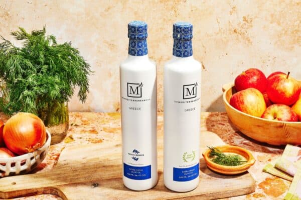 Greek extra virgin olive oil bundle on a table with onions, parsley and apples.