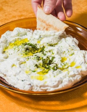 A pita wedge being dipped into a bowl of Maast O'Khiar garnished with dried mint and a drizzle of olive oil.