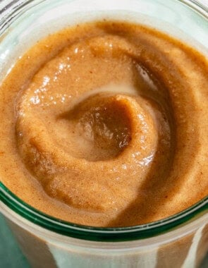 Date Caramel in a jar sitting on a cloth napkin surrounded by some dates and a spoon.