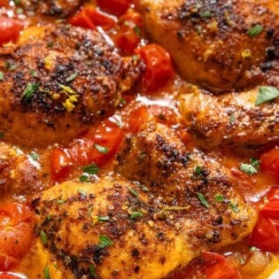 A closeup of chicken thighs in a cherry tomato sauce in a skillet.
