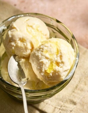 Scoops of olive oil ice cream topped with flaky sea salt and a drizzle of olive oil in a bowl with a spoon.
