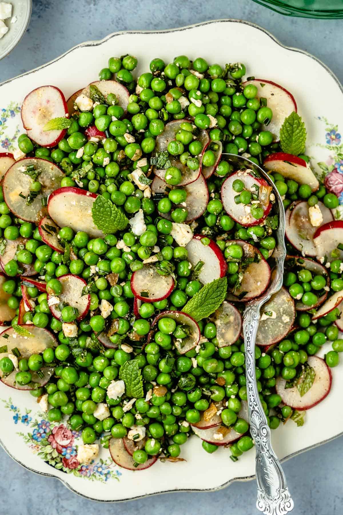 A bright, vibrant no-mayo spring pea salad with sliced radishes and mint on a floral plate with a silver serving spoon.