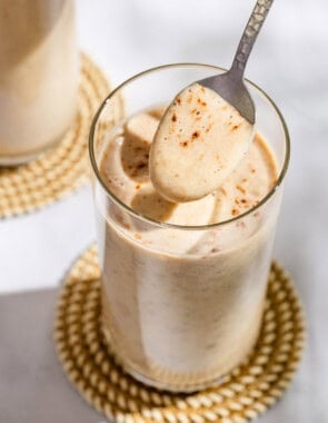 A spoonful of the date shake being held above a glass with the rest of the shake on a coaster.