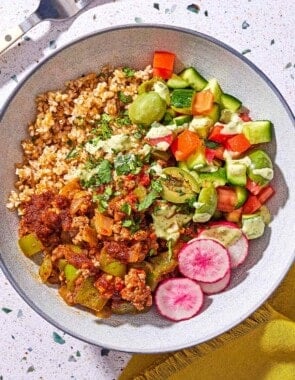A Mediterranean beef bowl next to a fork and a cloth napkin.