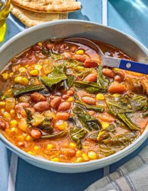 Collard green soup in a bowl with a spoon. Next to this is a kitchen towel and pieces of pita bread.