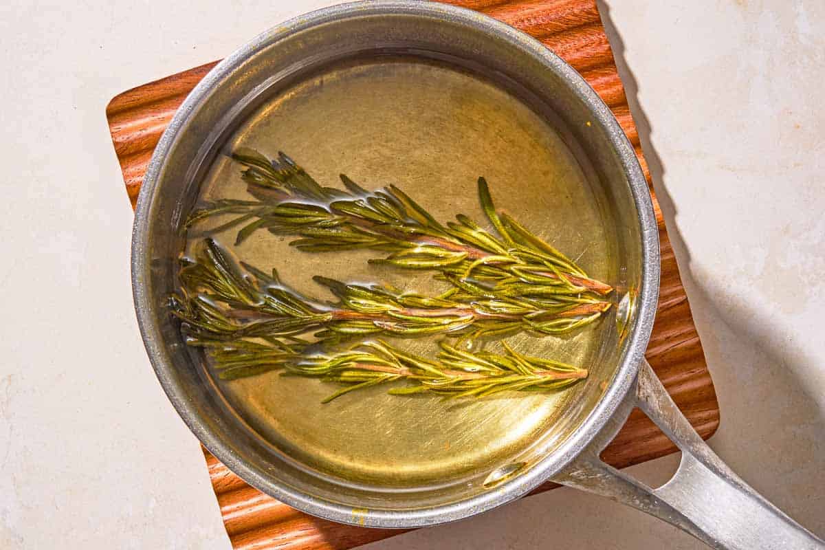 The simple syrup with sprigs of rosemary in a saucepan on a trivet.