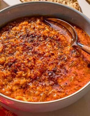 Turkish lentil stew topped with infused olive oil in a bowl with a spoon.