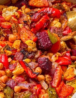 Oven roasted vegetables in a baking dish with a serving spoon.