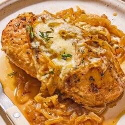 A serving of french onion chicken on a plate with a knife and fork.
