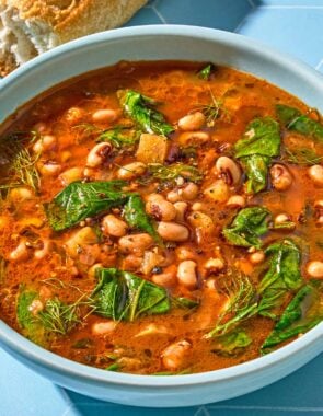 A serving of black eyed peas in a bowl next to a baguette.