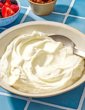 Homemade greek yogurt in a bowl with a spoon next to a small bowl with various berries and a bowl of granola.