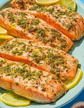 Four cooked lemon pepper salmon fillets on a platter with lemon wheels.