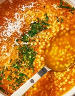 an overhead photo of a serving of pastina soup garnished with parsley and parmesan cheese in a bowl with a spoon.