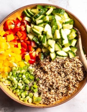 the ingredients for the quinoa salad in a serving bowl just before being mixed together with a wooden spoon.
