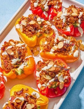 The quinoa stuffed peppers drizzled with tahini sauce in a baking dish.
