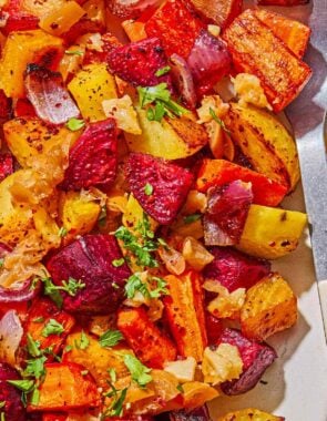 A close up of roasted root vegetables on a platter with a serving spoon.