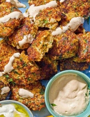 Shrimp kofta drizzled with tahini sauce on a platter with bowls of tahini and tzaziki sauce and lemon wedges.