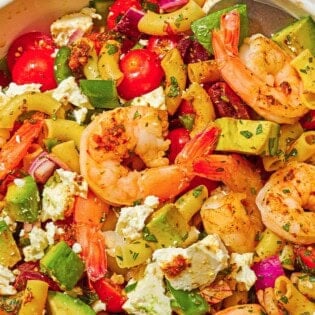 A bowl of shrimp pasta salad with a serving spoon next to a cloth napkin and a plate.