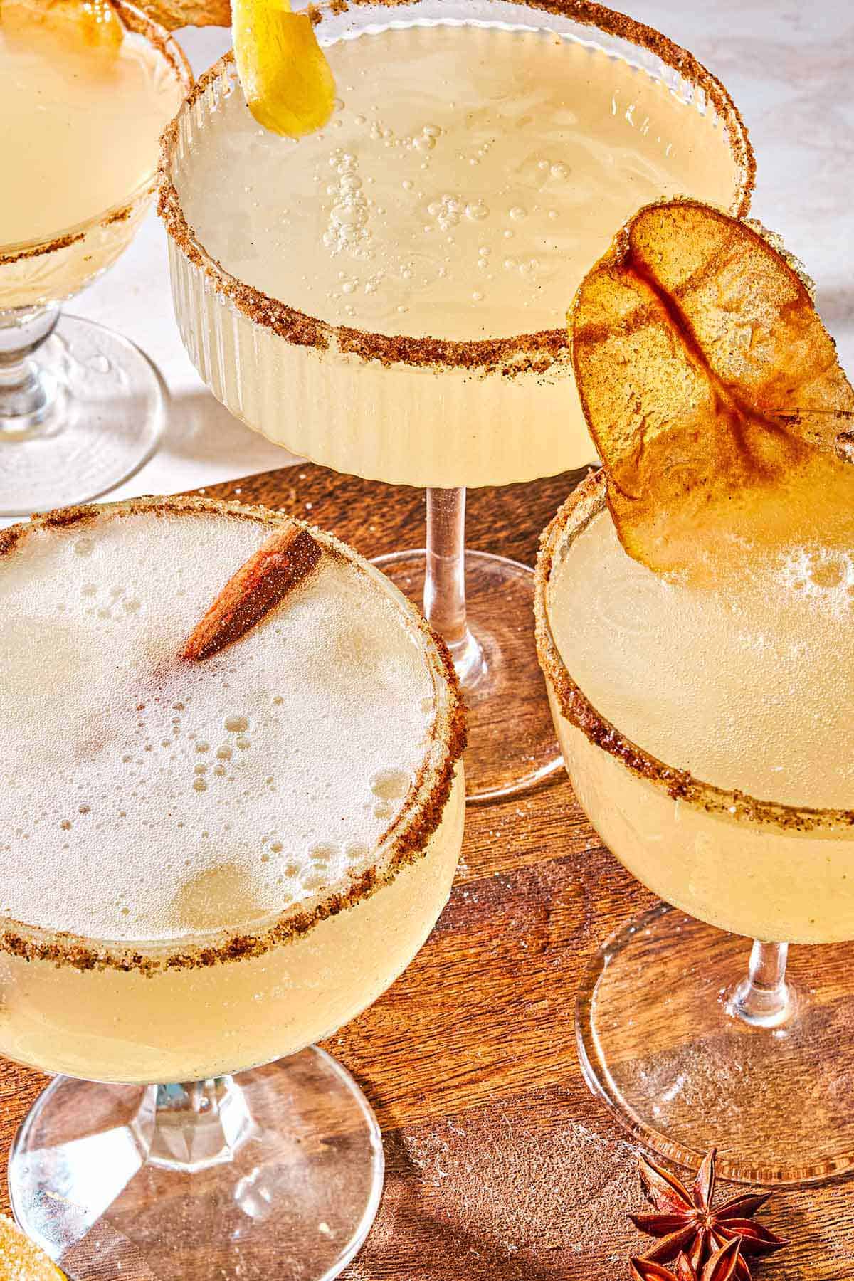 3 ginger beer mocktails, one garnished with a candied pear chip and one with a cinnamon stick, on a wooden platter.