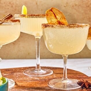 Three ginger beer mocktails on a wooden platter with a bowl of crystalized ginger pieces. In the background is another mocktail.
