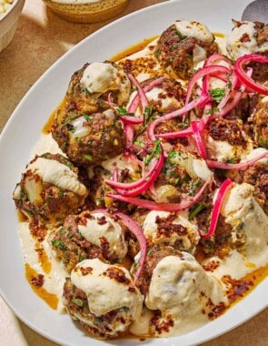 The turkish meatballs and yogurt sauce topped with pickled red onions and chopped parsley on a platter next to a bowl pickled red onions.