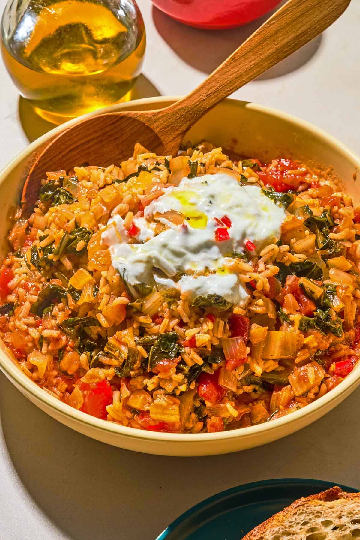 The swiss chard recipe topped with yogurt and olive oil in a serving bowl with a wooden spoon next to a bottle of olive oil.
