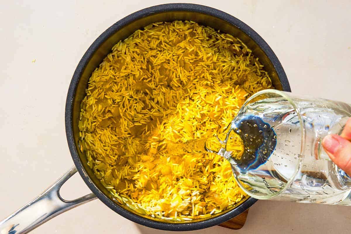 Water being poured into the saucepan with the rice and aromatics.