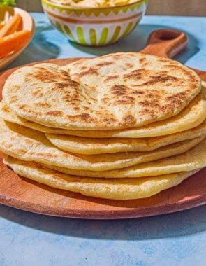 6 pieces of the flatbread recipe on a wooden serving board. Next to this is a bowl of hummus.